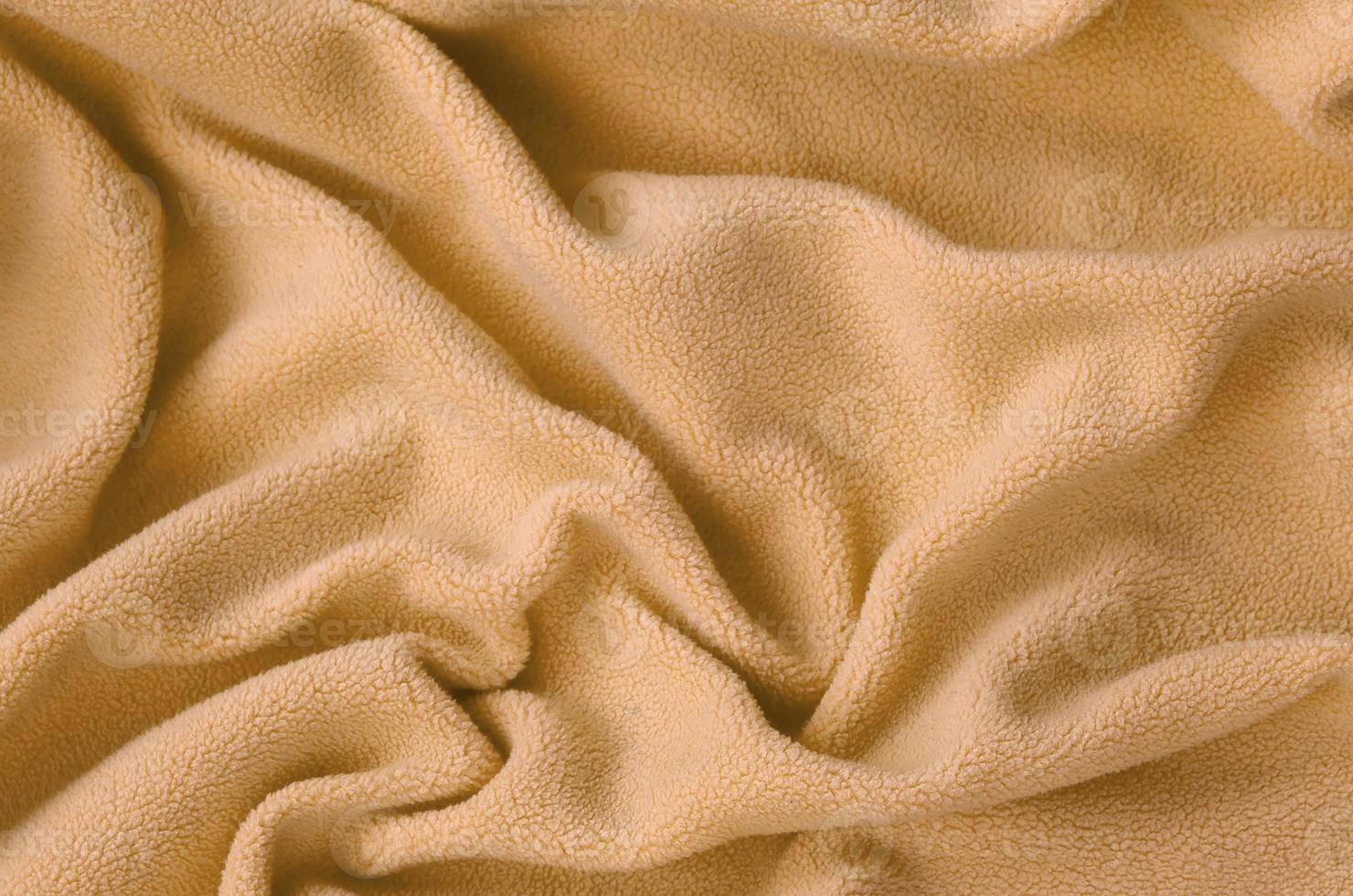 The blanket of furry orange fleece fabric. A background of light orange soft plush fleece material with a lot of relief folds photo