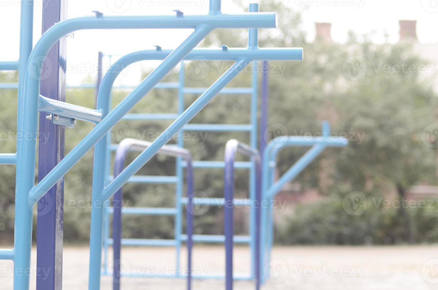 Sports bars in blue on the background of a street sports ground for training in athletics. Outdoor athletic gym equipment. Macro photo with selective focus and extremely blurred background