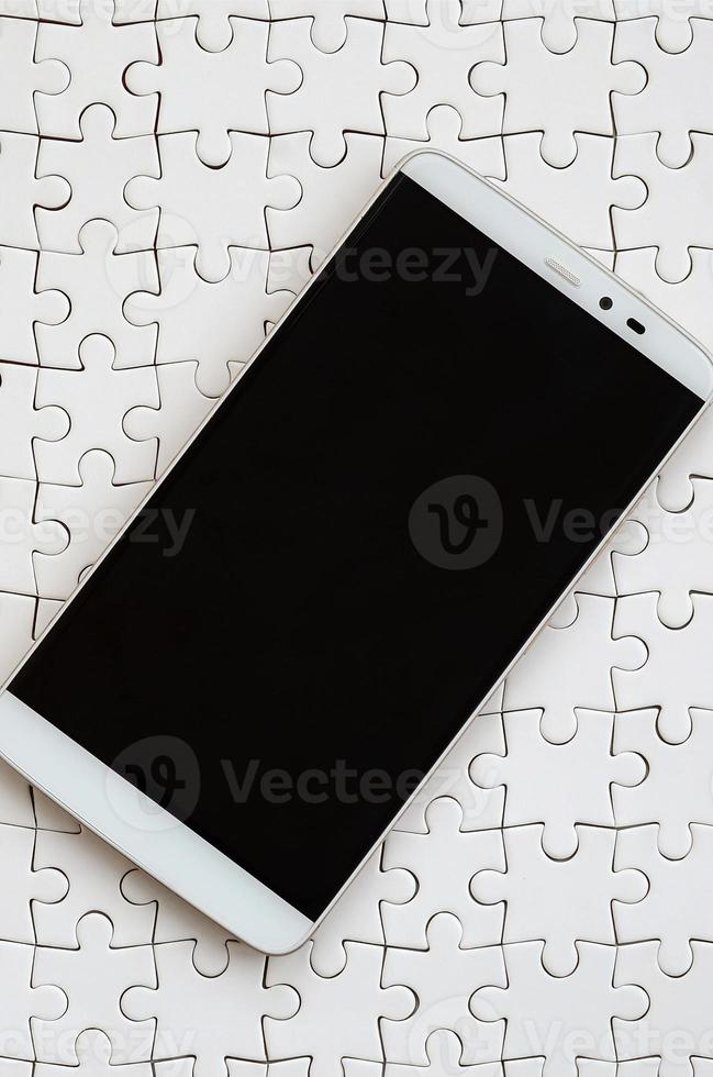 A modern big smartphone with a touch screen lies on a white jigsaw puzzle in an assembled state photo