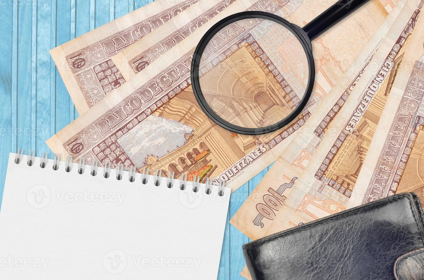 100 Guatemalan quetzales bills and magnifying glass with black purse and notepad. Concept of counterfeit money. Search for differences in details on money bills to detect fake photo