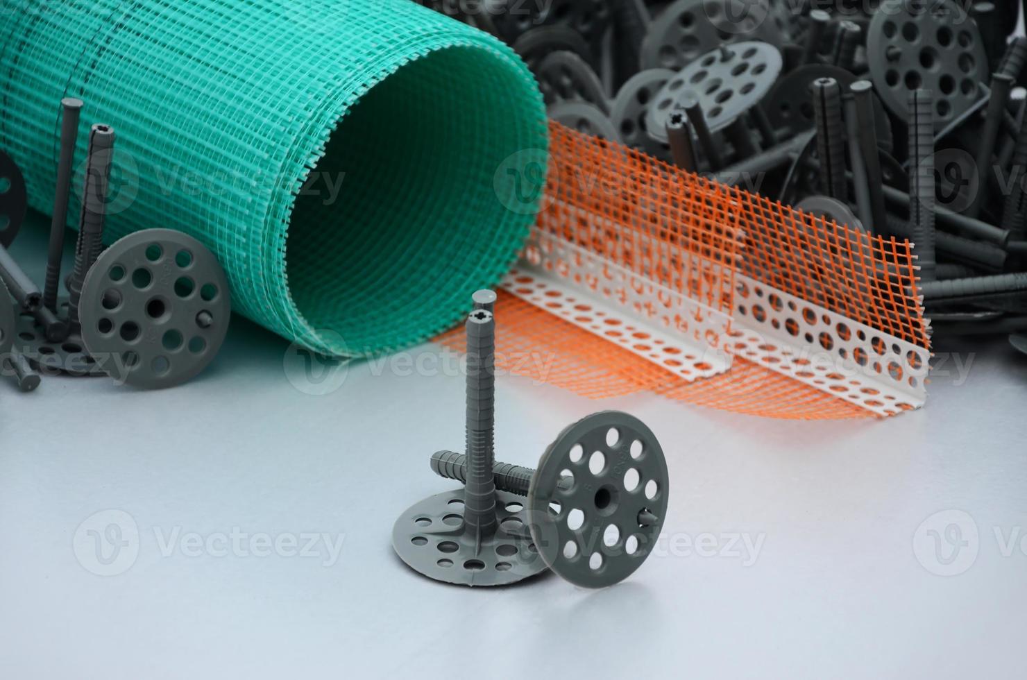 A set of construction items for the insulation of walls. Plastic dowels, a roll of mesh for the insulation of facades and a corner profile with a grid lie on the foam polystyrene surface photo
