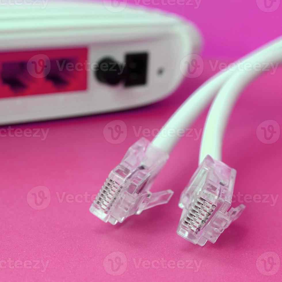 el enrutador de Internet y los enchufes del cable de Internet se encuentran sobre un fondo rosa brillante. elementos necesarios para internet foto