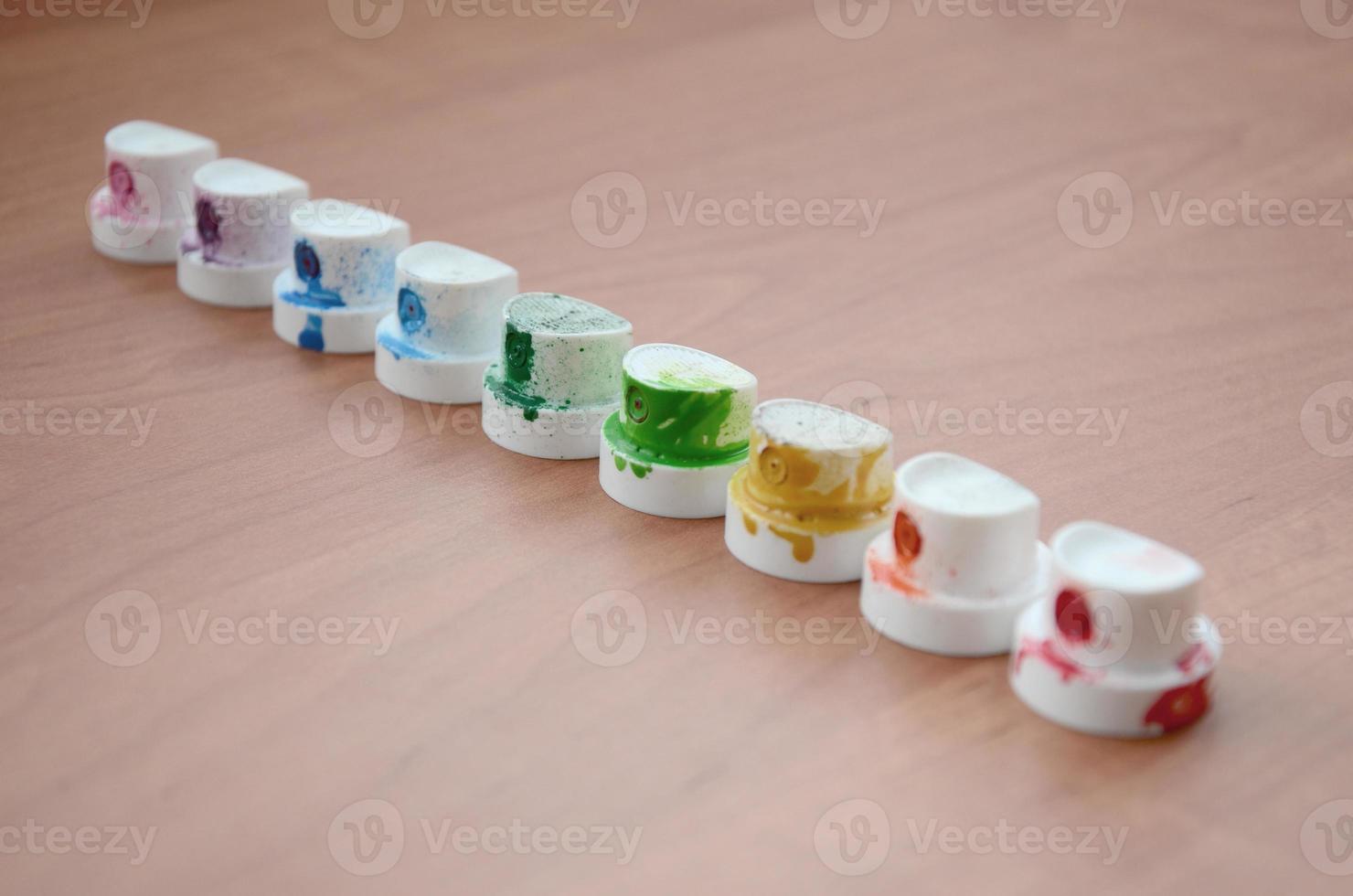 The soiled multicolored nozzles from the paint sprayer are lined up on a wooden table. Street art concept photo