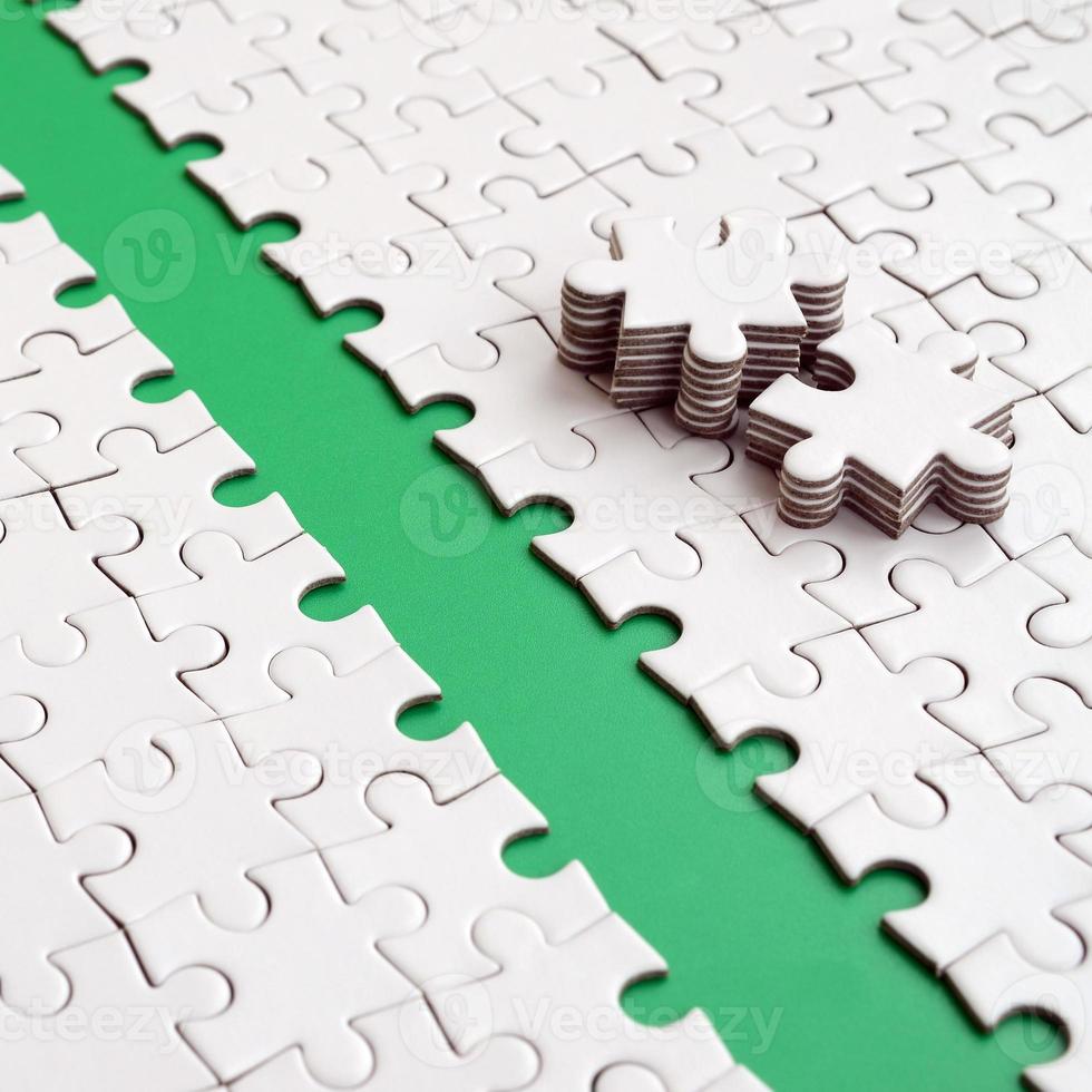 The green path is laid on the platform of a white folded jigsaw puzzle. The missing elements of the puzzle are stacked nearby. Texture image with space for text photo