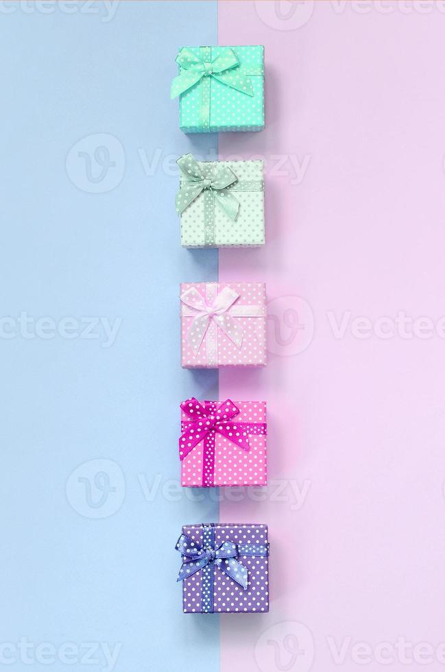 Small gift boxes of different colors with ribbons lies on a violet and pink background photo