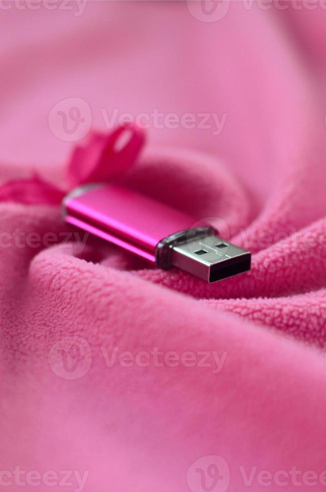 Brilliant pink usb flash memory card with a pink bow lies on a blanket of soft and furry light pink fleece fabric with a lot of relief folds. Memory storage device in women's design photo