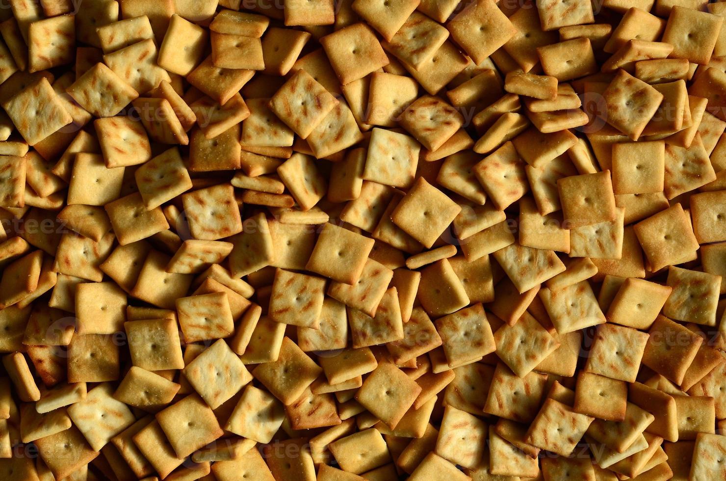 Background texture of small edible squares baked from dough and sprinkled with salt. A lot of salt cracker photo