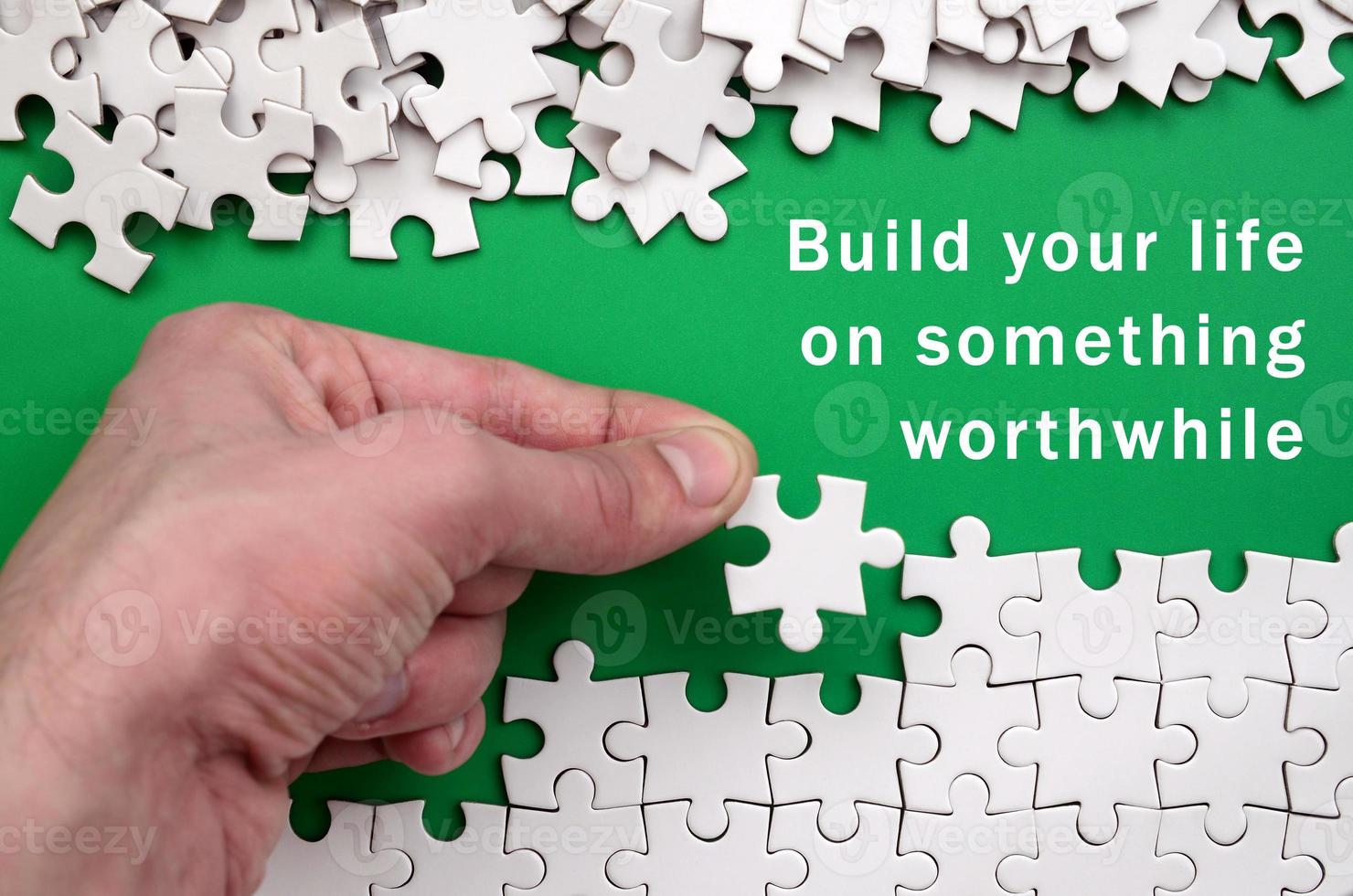 Build your life on something worthwhile. The hand folds a white jigsaw puzzle and a pile of uncombed puzzle pieces lies against the background of the green surface photo