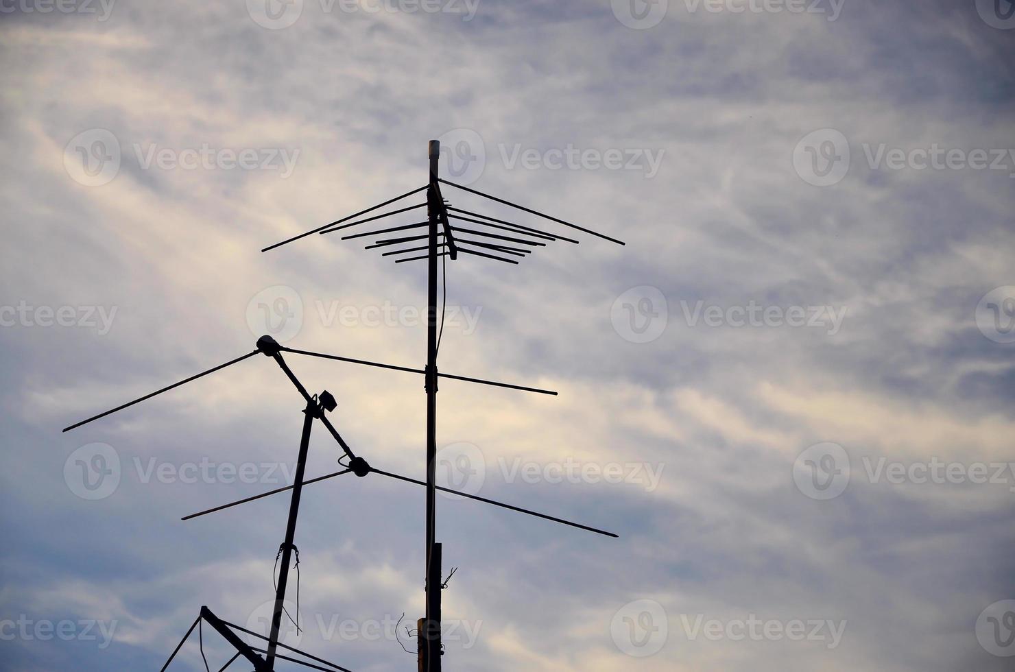 An old and rusty television antenna against a cloudy blue sky photo
