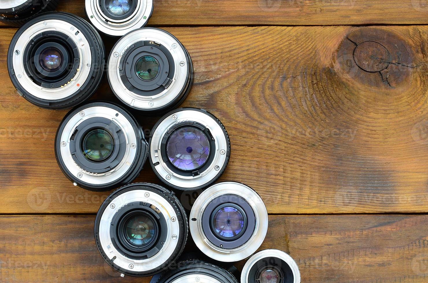 Several photographic lenses lie on a brown wooden background. Space for text photo