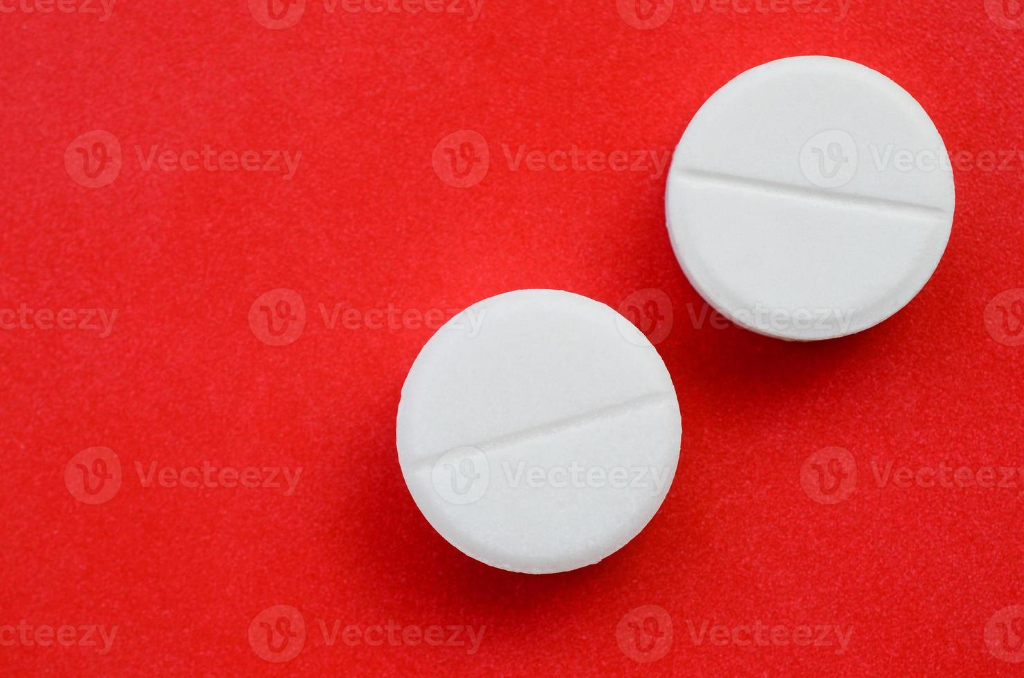 A few white tablets lie on a bright red background surface. Background image on medical and pharmaceutical topics photo