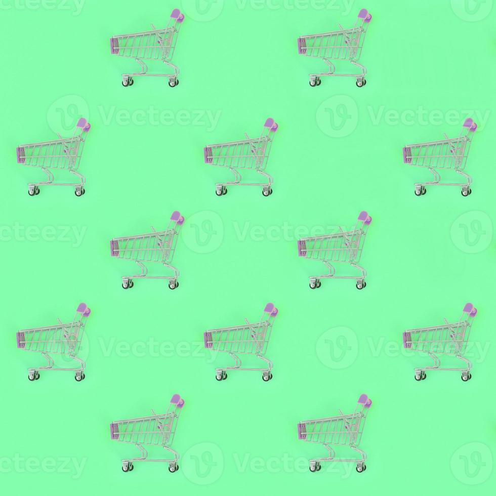 Shopping addiction, shopping lover or shopaholic concept. Many small empty shopping carts perform a pattern on a pastel colored paper background. Flat lay composition, top view photo