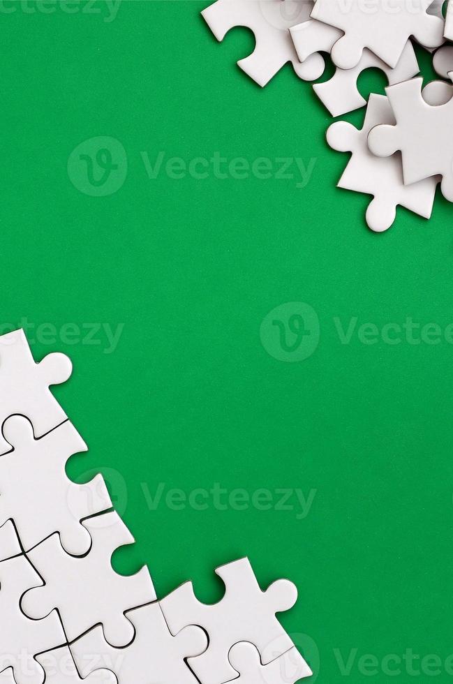 Fragment of a folded white jigsaw puzzle and a pile of uncombed puzzle elements against the background of a green surface. Texture photo with space for text