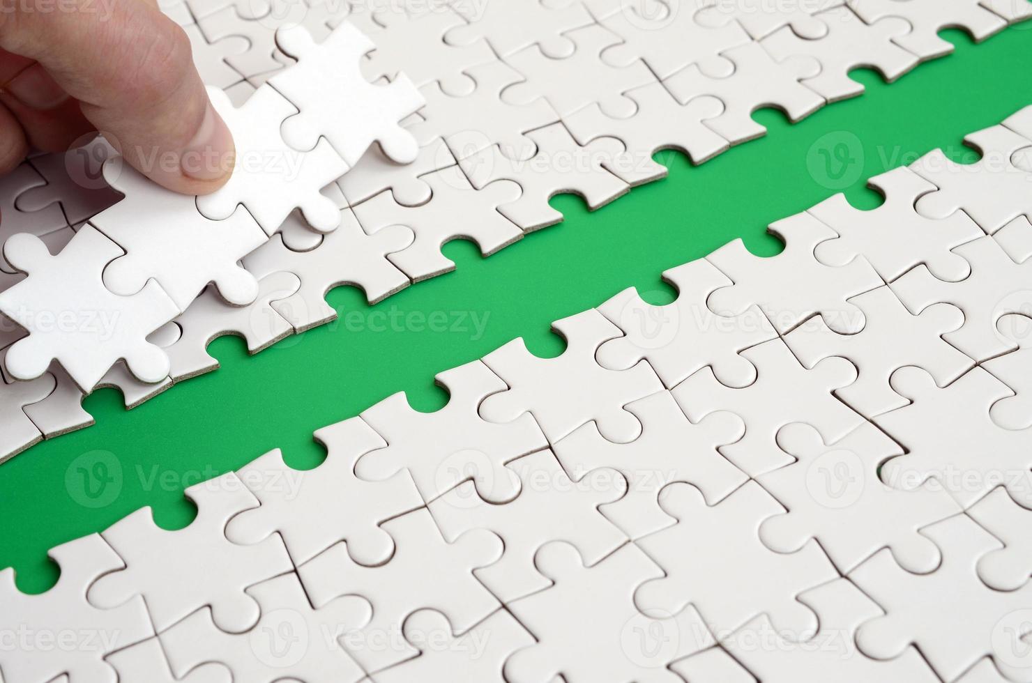 The human hand paves the way to the surface of the jigsaw puzzle, forming a green space. The concept of overcoming the difficulties on the way to success photo