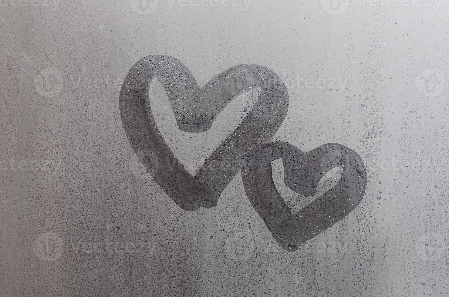 Couple of abstract blurred love heart symbol drawn by hand on the wet window glass with sunlight background. Template for Valentine Day postcards photo