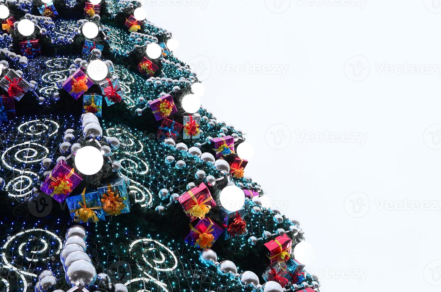 A fragment of a huge Christmas tree with many ornaments, gift boxes and luminous lamps. Photo of a decorated Christmas tree close-up with copy space