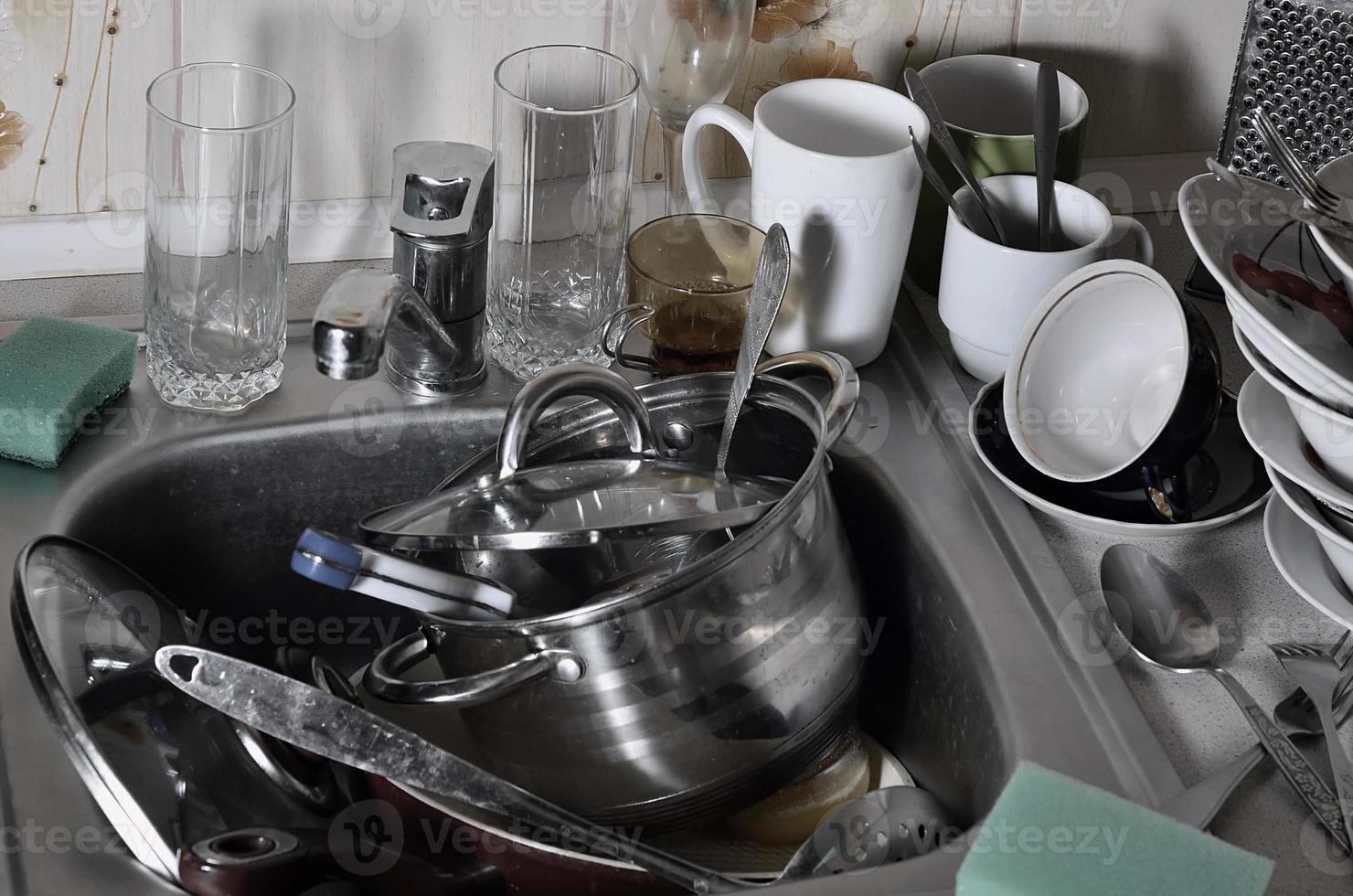 A huge pile of unwashed dishes in the kitchen sink and on the countertop photo
