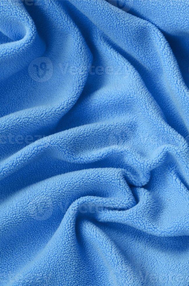 The blanket of furry blue fleece fabric. A background of light blue soft plush fleece material with a lot of relief folds photo
