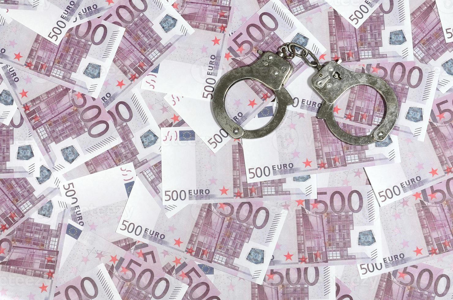 Handcuffs on five hundred euros background. Financial crime, dirty money and corruption concept - 500 money bills and dirty steel handcuffs photo