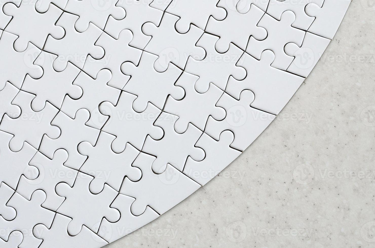 A white jigsaw puzzle in the complete form lies on a treated stone surface. Textured image with copy space photo