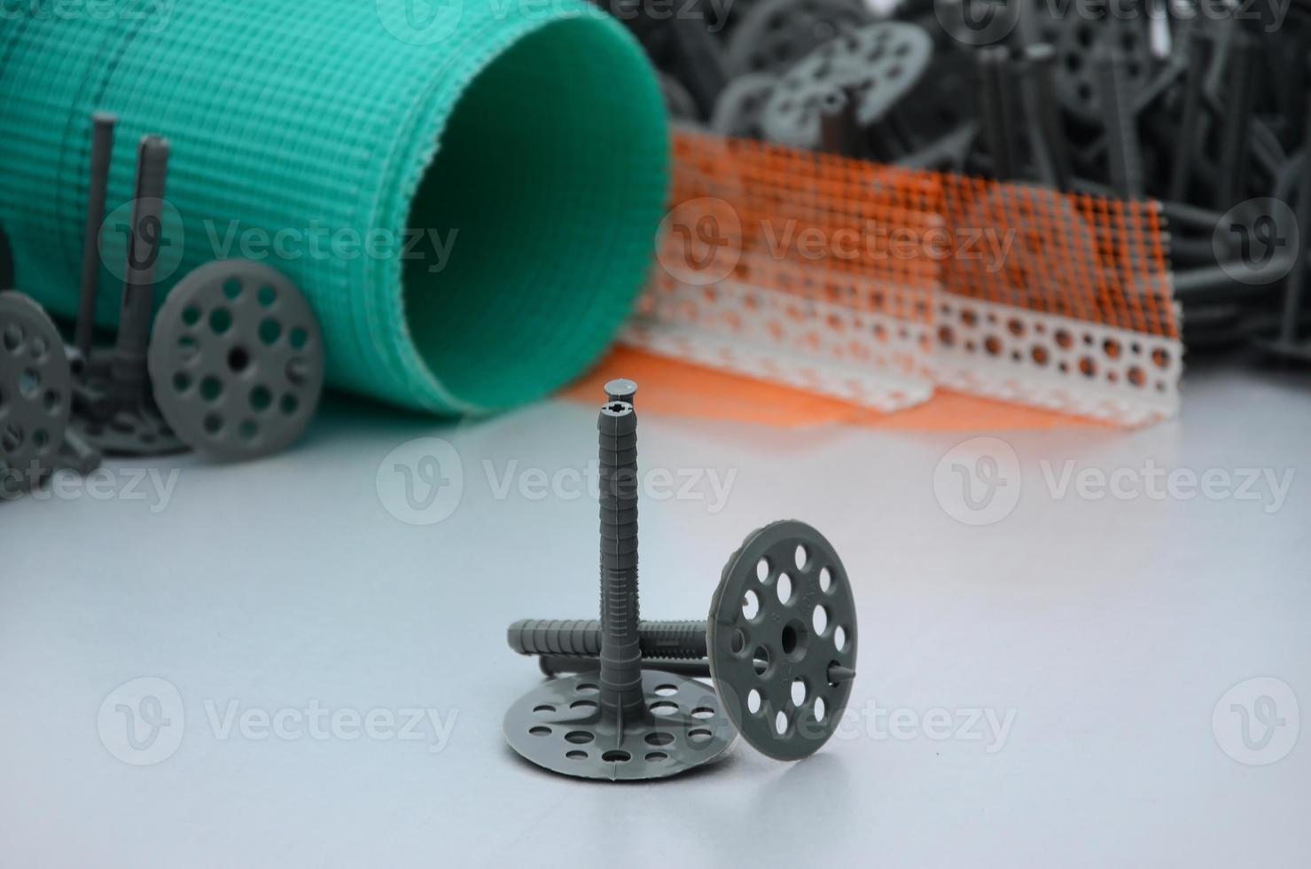 A set of construction items for the insulation of walls. Plastic dowels, a roll of mesh for the insulation of facades and a corner profile with a grid lie on the foam polystyrene surface photo