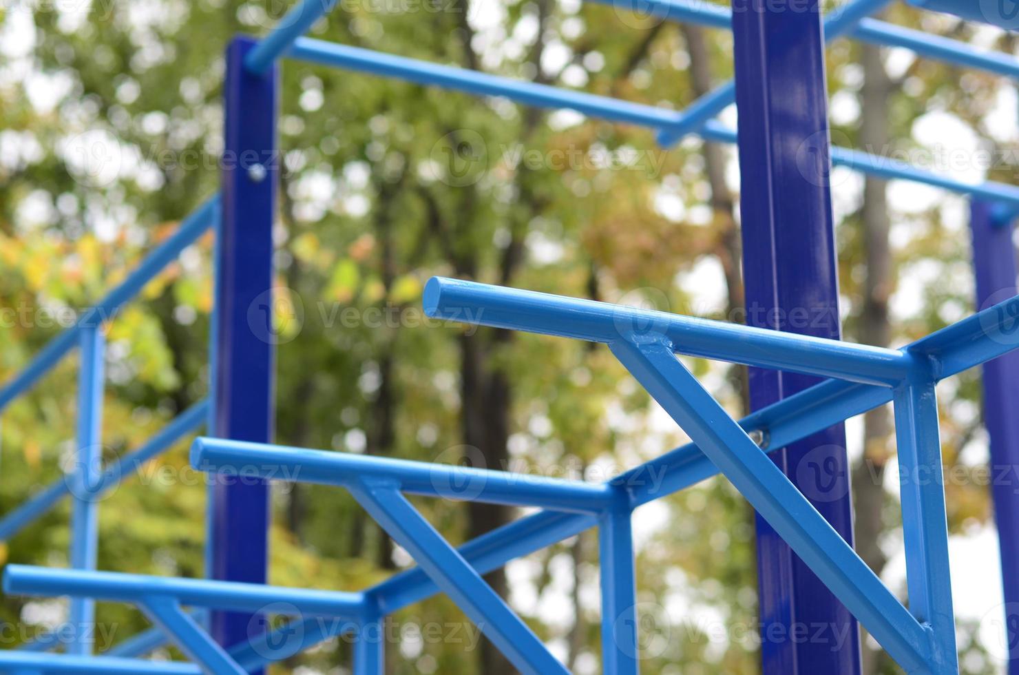 Blue metal pipes and cross-bars against a street sports field for training in athletics. Outdoor athletic gym equipment. Macro photo with selective focus and extremely blurred background