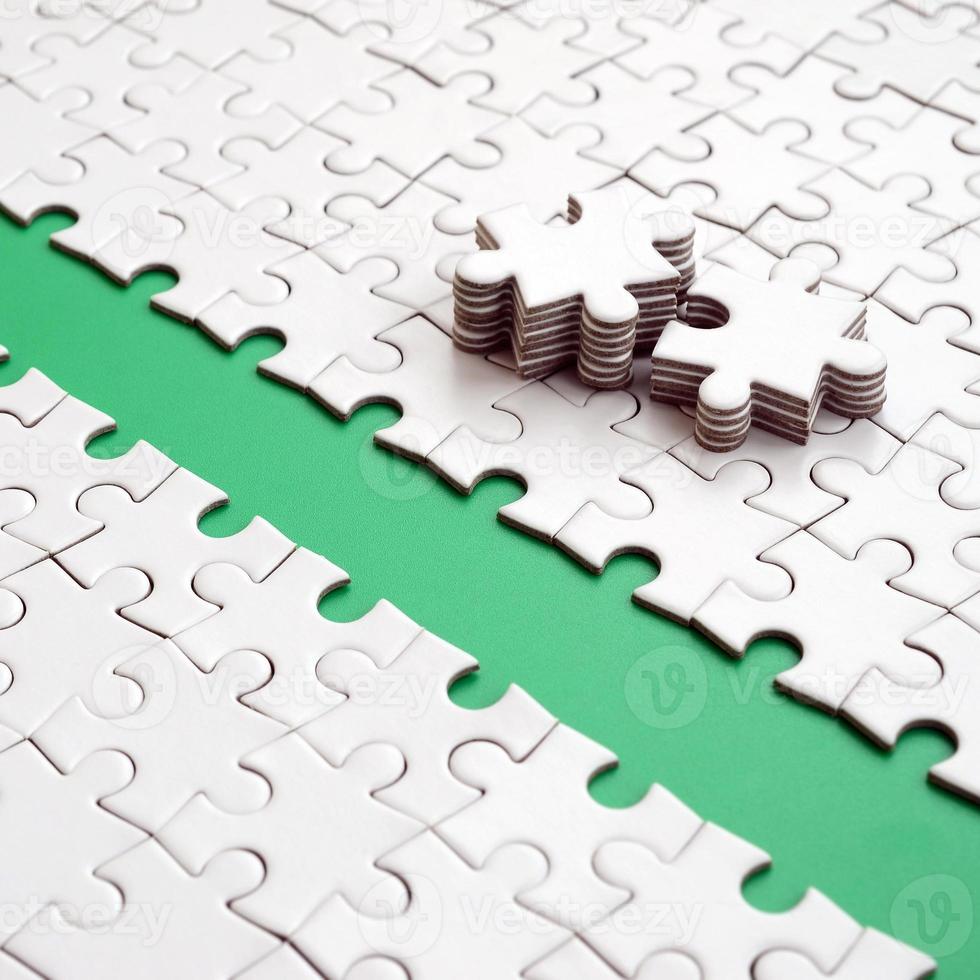 The green path is laid on the platform of a white folded jigsaw puzzle. The missing elements of the puzzle are stacked nearby. Texture image with space for text photo