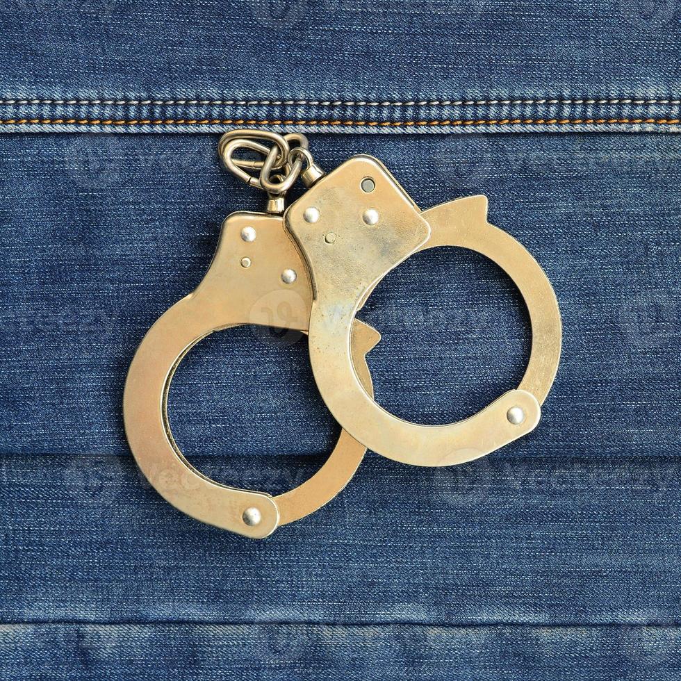 Police steel handcuffs lying on dark blue jeans background photo