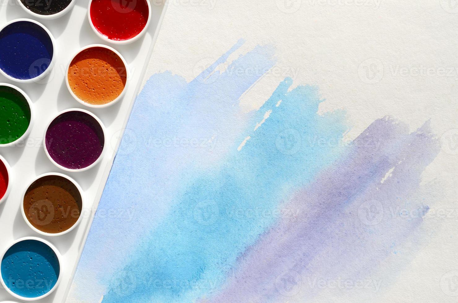 A new set of watercolors lies on a sheet of paper, which shows an abstract watercolor drawing in the form of blue strokes. The concept of amateur painting among teenagers photo