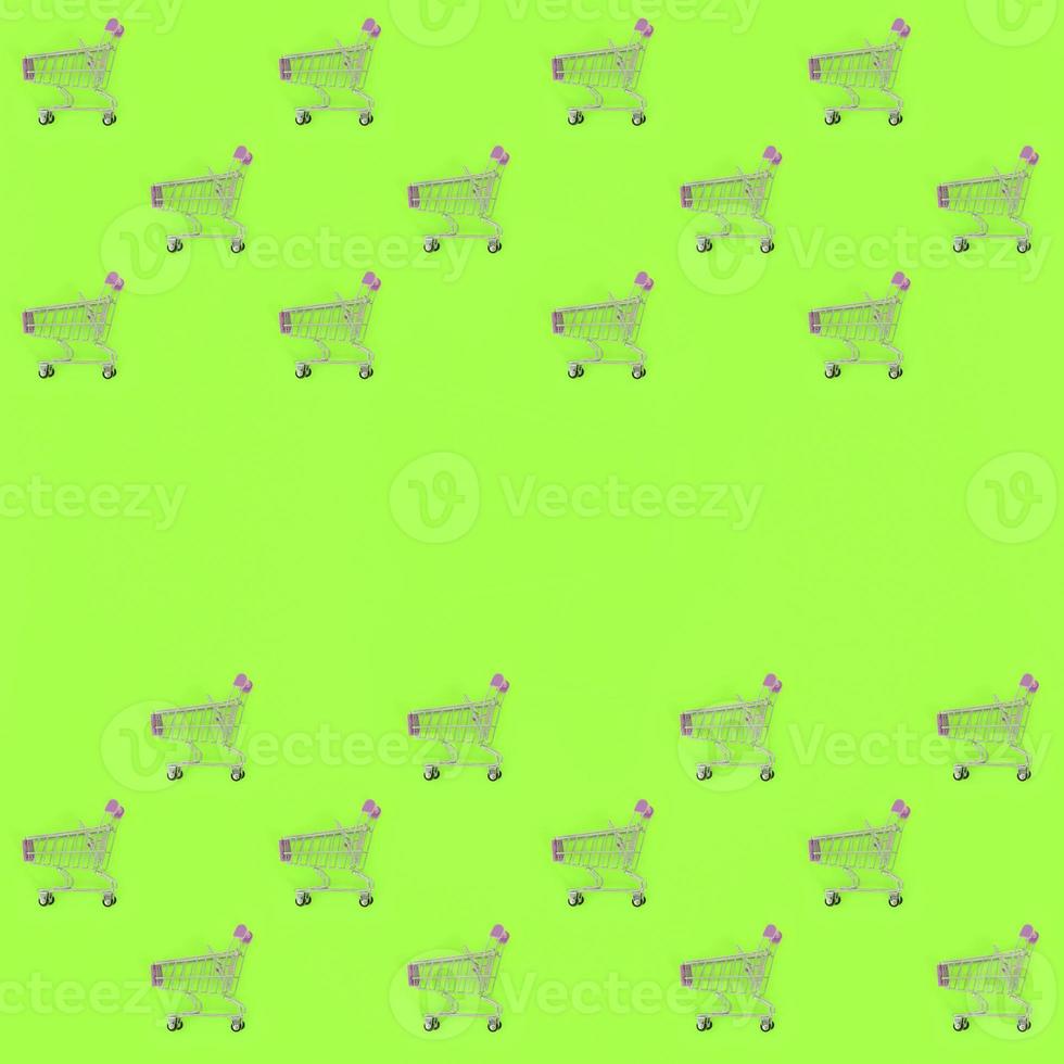 Shopping addiction, shopping lover or shopaholic concept. Many small empty shopping carts perform a pattern on a pastel colored paper background. Flat lay composition, top view photo