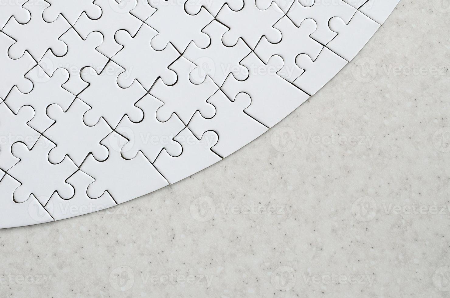 A white jigsaw puzzle in the complete form lies on a treated stone surface. Textured image with copy space photo