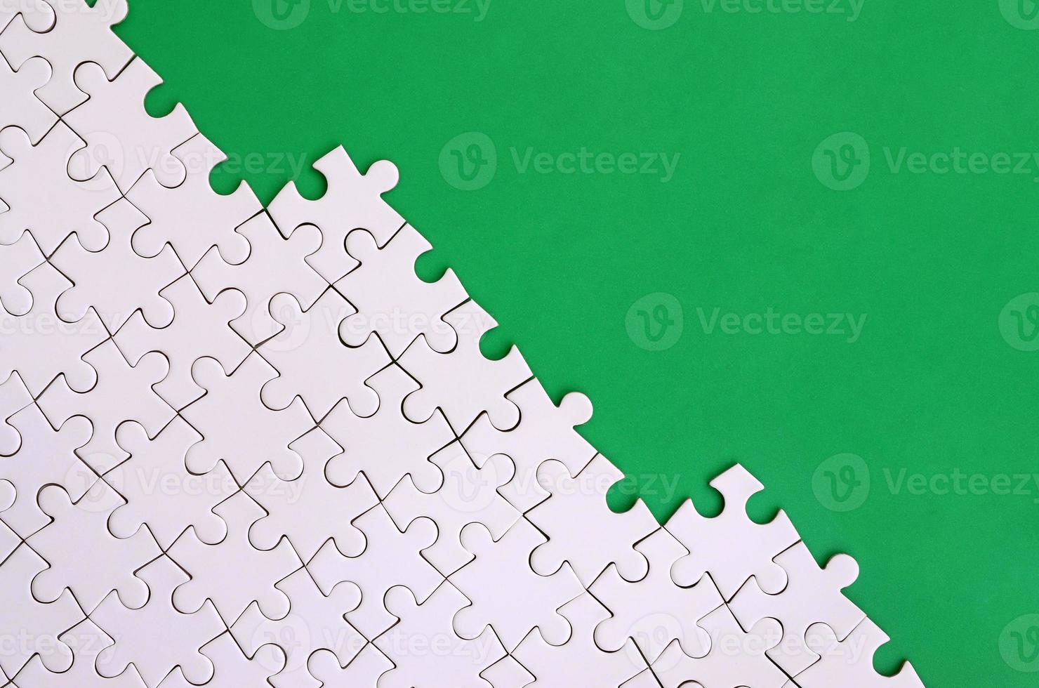 Fragment of a folded white jigsaw puzzle on the background of a green plastic surface. Texture photo with copy space for text