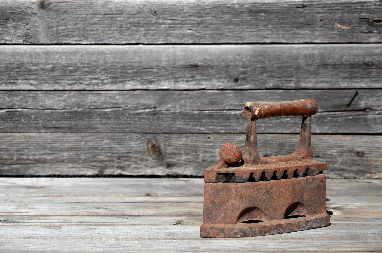 The heavy and rusty old coal iron lies on a wooden surface photo