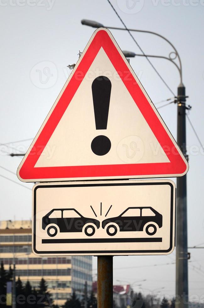 High risk of collision. A road sign with an exclamation point and two cars that crashed into each other photo