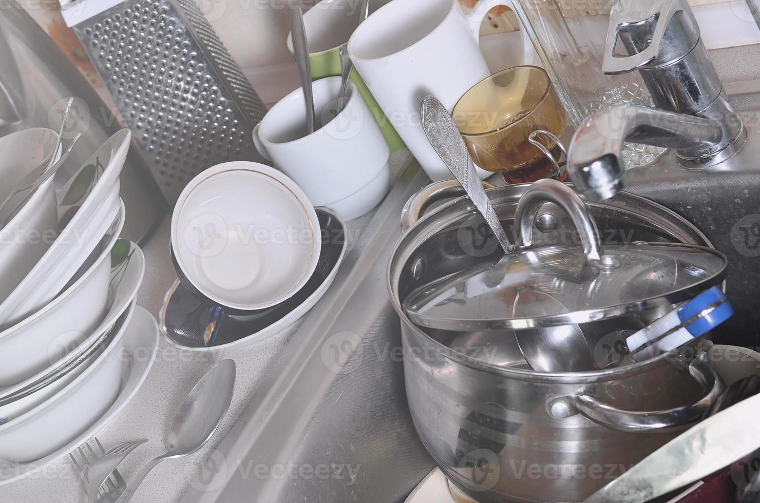 A huge pile of unwashed dishes in the kitchen sink and on the countertop photo