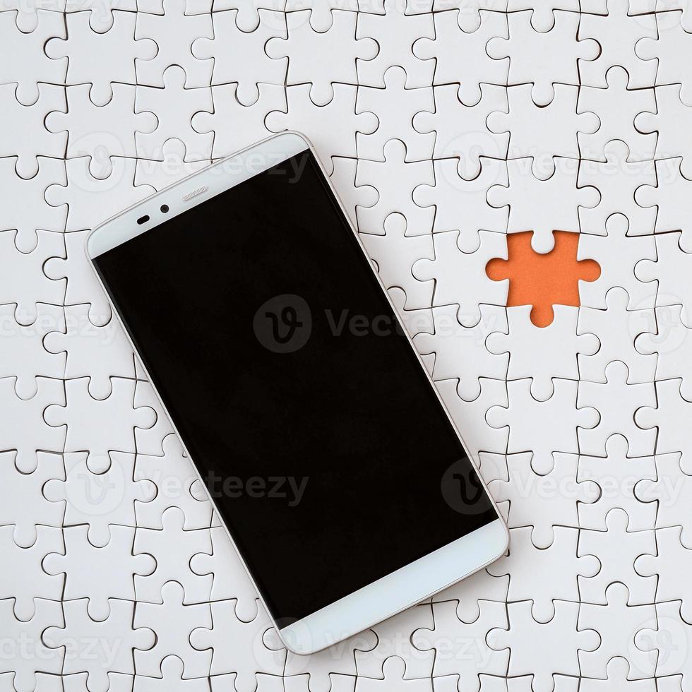 A modern big smartphone with a touch screen lies on a white jigsaw puzzle in an assembled state photo