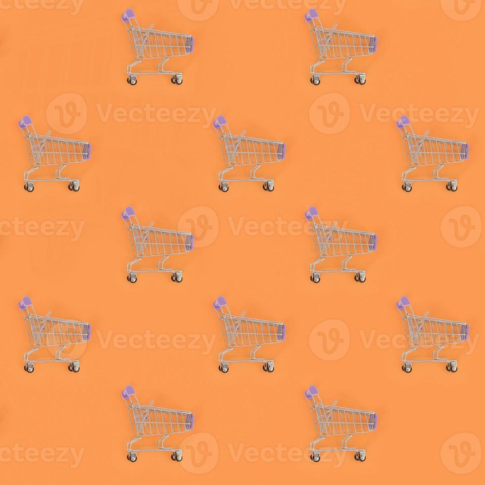 Shopping addiction, shopping lover or shopaholic concept. Many small empty shopping carts perform a pattern on a pastel colored paper background. Flat lay composition, top view photo