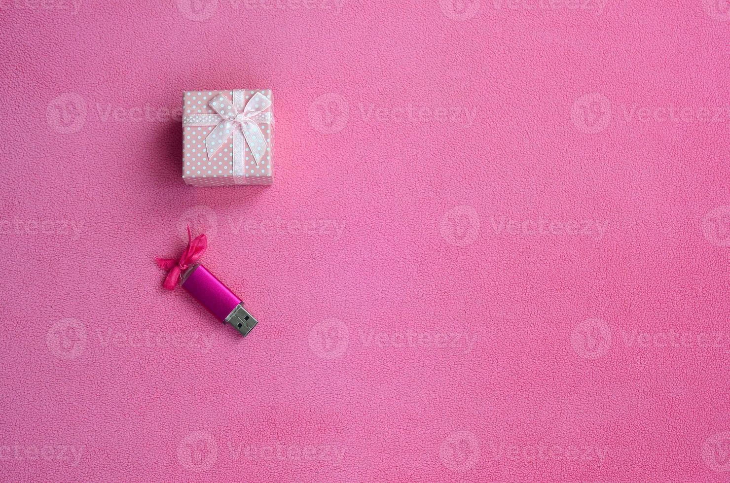 Brilliant pink usb memory card with a pink bow lies next to a small gift box in pink with a small bow on a blanket of soft and furry light pink fleece fabric. Classic female gift memory card design photo