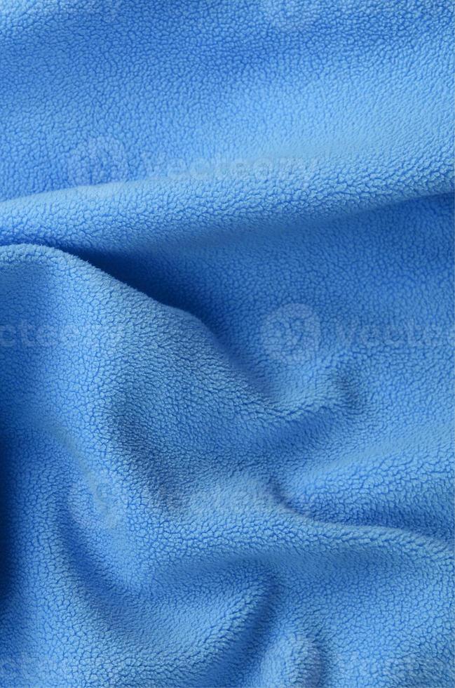 The blanket of furry blue fleece fabric. A background of light blue soft plush fleece material with a lot of relief folds photo