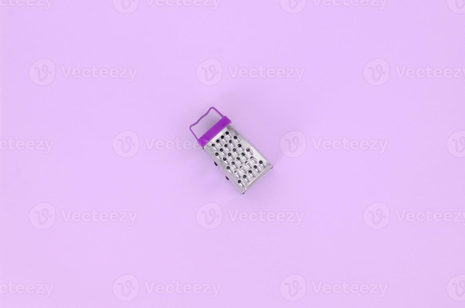 Stainless steel grater lies on a pastel colored paper. Kitchen accessories. Tools for cooking. Flat lay top view photo