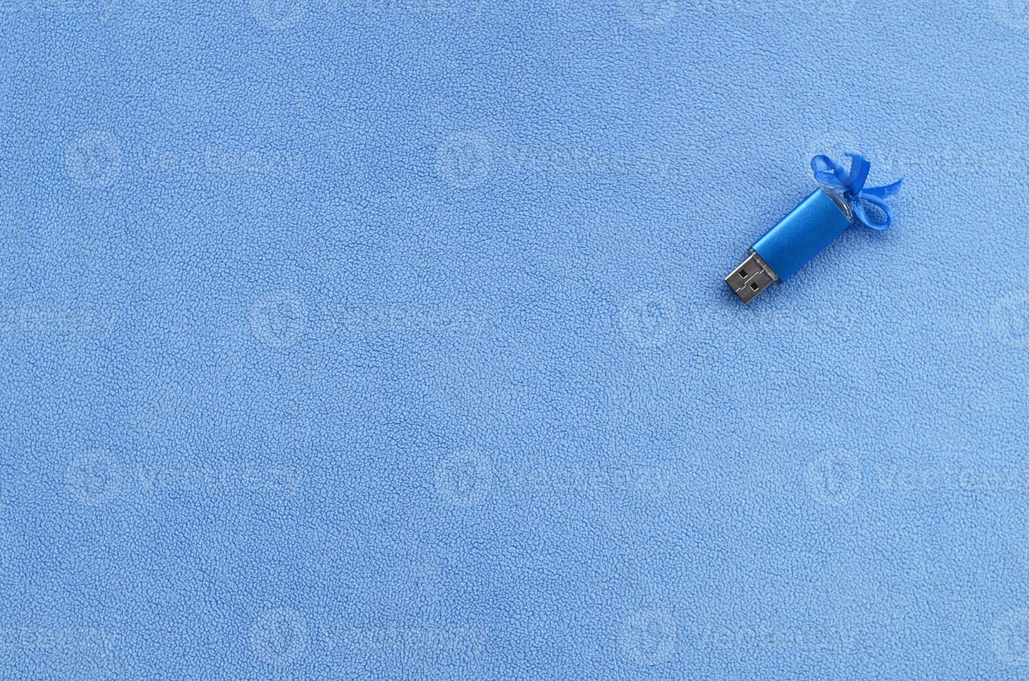 Brilliant blue usb flash memory card with a blue bow lies on a blanket of soft and furry light blue fleece fabric. Classic female gift design for a memory card photo