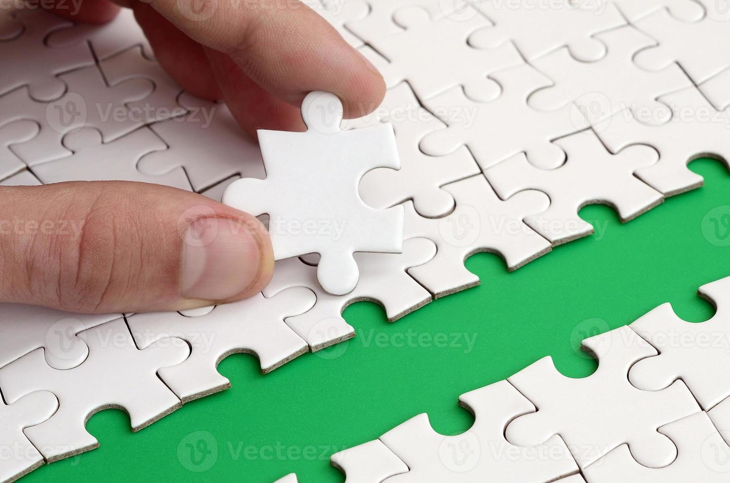 The human hand paves the way to the surface of the jigsaw puzzle, forming a green space. The concept of overcoming the difficulties on the way to success photo