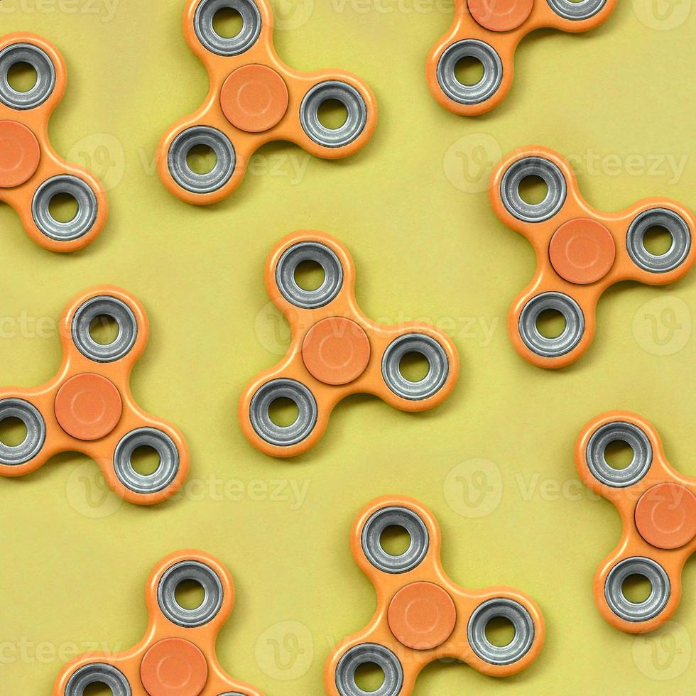 Many orange fidget spinners lies on texture background of fashion pastel orange color paper photo