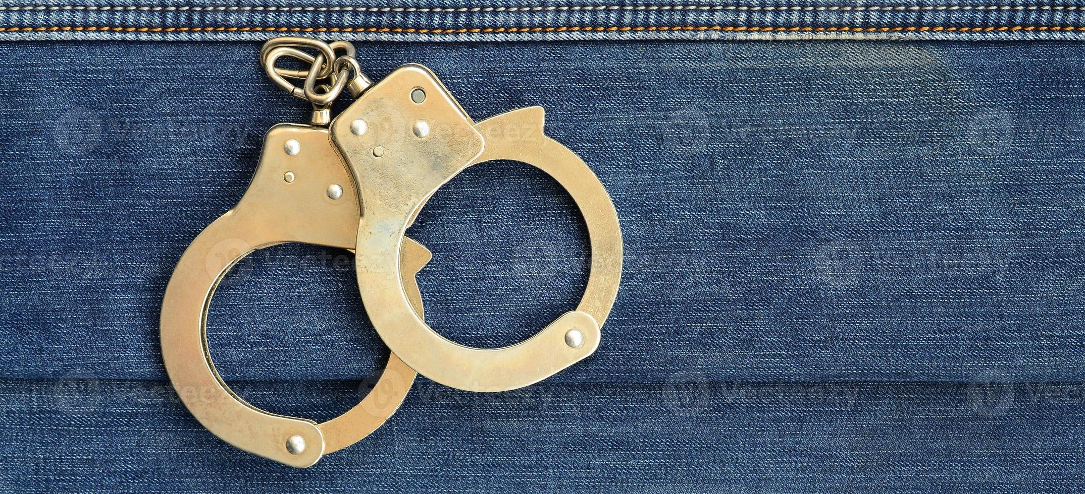 Police steel handcuffs lying on dark blue jeans background photo