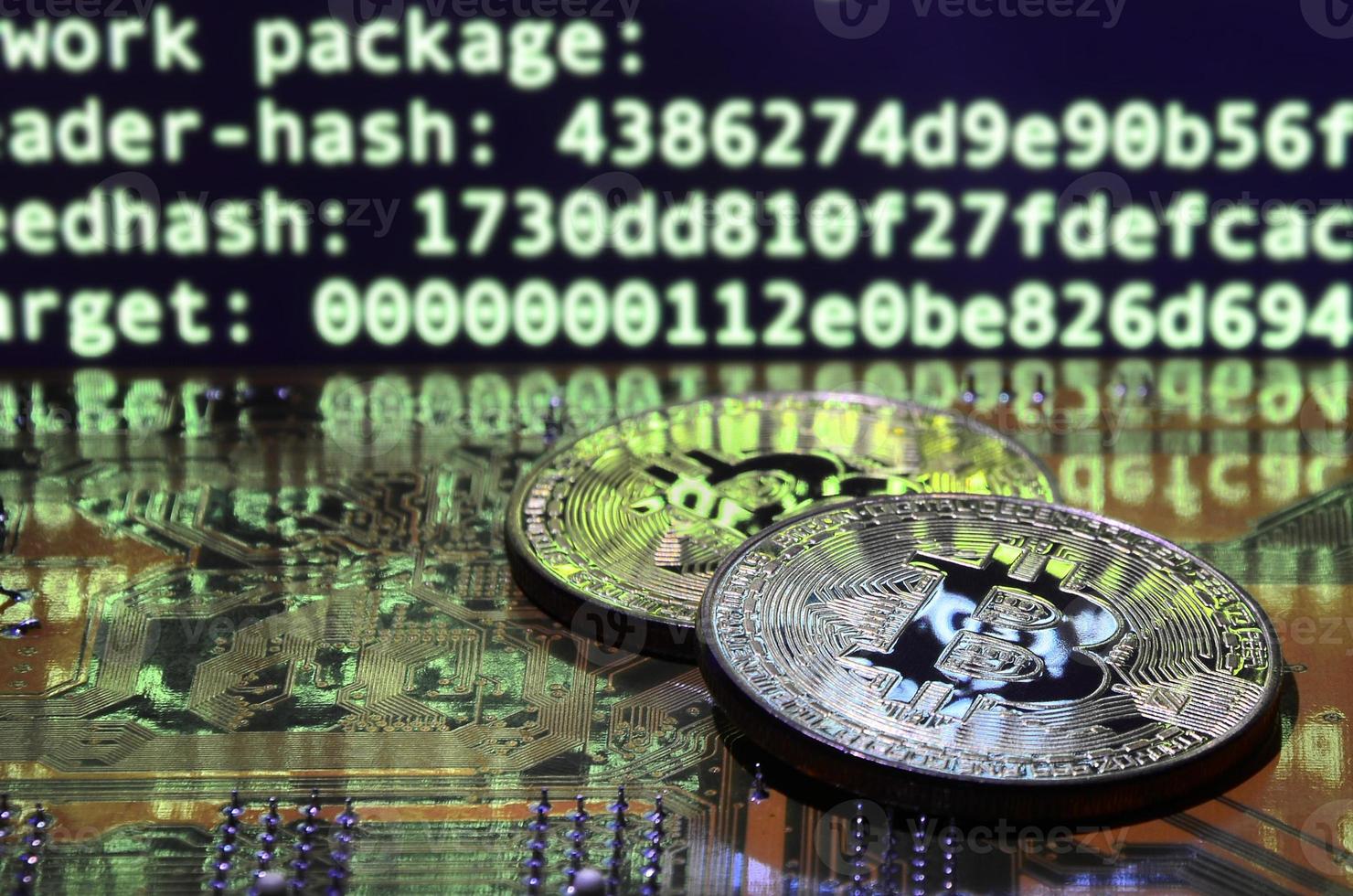 Two bitcoins lies on a videocard surface with background of screen display of cryptocurrency mining by using the GPUs photo