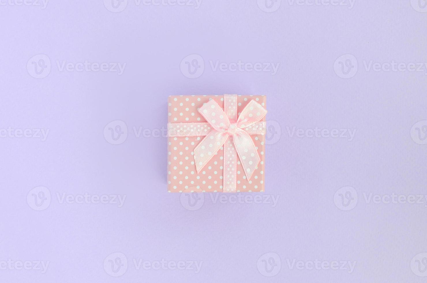 Small pink gift box with ribbon lies on a violet background. Minimalism flat lay top view photo