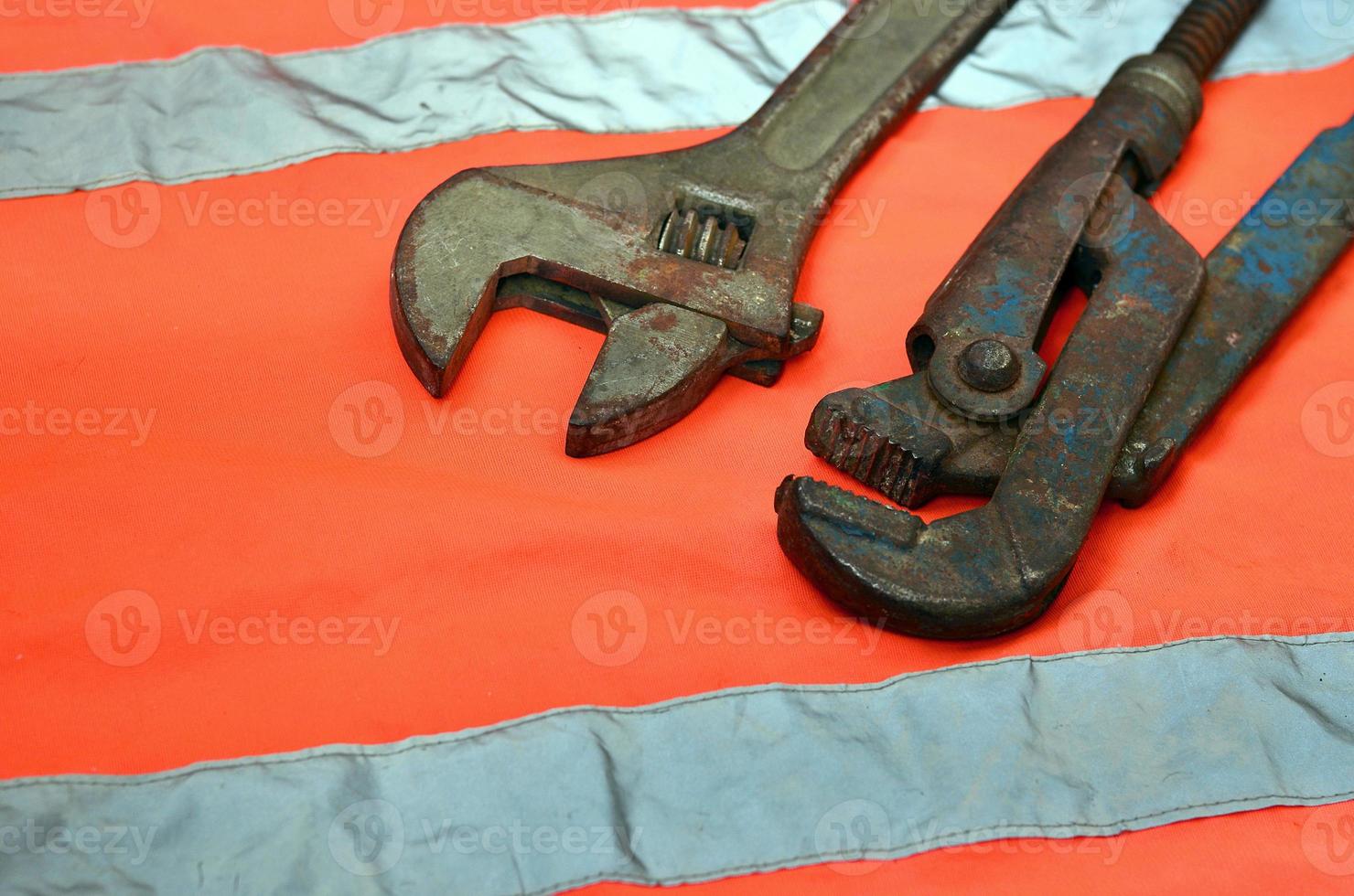 Adjustable and pipe wrenches against the background of an orange signal worker shirt photo