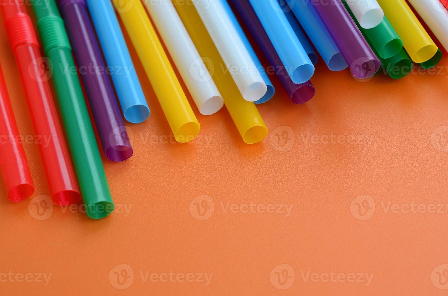 Many colorful straws for drinks lies on a bright orange background surface photo