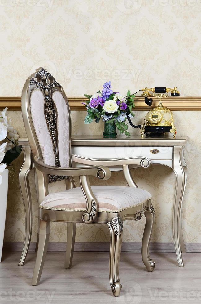 A fragment of a retro interior with a chair and a desk on which is located a telephone and a vase of flowers photo