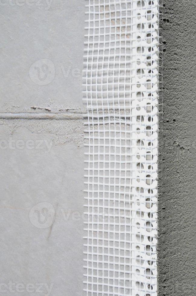 The texture of the wall, covered with gray polystyrene foam plates, which are coated with a reinforcing mixture with a plastic reinforcing profile corner. Stage of wall insulation photo